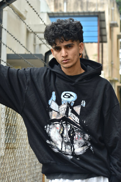 Person wearing a black hoodie with graphic design, standing outdoors.